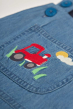 close up of red tractor embroidery applique detail on front of frugi chambray dungaree