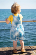 A child wearing the Frugi  Deep Sea Check/Crab Alby Dungaree with a yellow short sleeved t-short underneath  showing the back of their outfit 