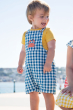 A child wearing the Frugi  Deep Sea Check/Crab Alby Dungaree with a yellow short sleeved t-short underneath 