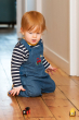 Young child on their knees on a wooden floor wearing the Frugi chambray tractor dungarees and playing with wooden trains