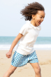 Child running on a beach wearing the Frugi Ada Collar T-Shirt and blue and white check shorts 