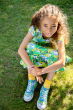 Child sitting down on grass wearing the Frugi Hedgerow print Spring Skater Dress