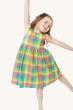 A child smiling with their arms outstretched doing a ballet pose, showing the twirly dress skirt of the Frugi Organic Arya Summer Dress - Summertime Check, on a cream background