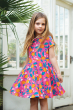 A child stood in front of a large green leafed plant, twirling the skirt section of the Frugi Organic Summer Skater Dress - Orange Blossom