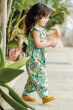 A child happily walking among trees, wearing the Frugi Children's Organic Cotton Etta Reversible Playsuit - Tropical Birds / Spring Dobby. A beautiful reversible play-suit, filled with colourful tropical birds and flowers on one side, and a plane mint gre
