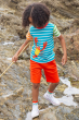 A child exploring the rock-pools at the beach, wearing the Frugi Children's Organic Cotton Hotchpotch Applique T-Shirt - Lobster. A colourful multi stripe Frugi T-Shirt for children, made from organic cotton and features a playful Lobster applique on the 