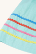 A closer look at the colourful piping on the skirt section of the dress in blue, red, pink and yellow, of the Frugi Organic Phebe Party Dress - Spring Mint / Macaw. On a cream background