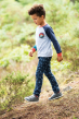 Child wearing the Frugi Forest printed Jordan jeans with  raglan t-shirt, grey trainers walking through the woods
