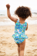 Child on a beach wearing the Frugi Postcards design Little Coral Swimsuit showing the back on the swimsuit