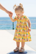 Young toddler wearing the Frugi Dara Baby Body Dress with a yellow Rainbow Sprinkles design pictured on a plain background holding an adults hand