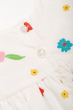 Close up of the button closure on the back of the Frugi Soft White Flowers Elowen Dress pictured on a plain background