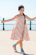 Child wearing the Frugi Tallulah Beach Stripe Trapeze Dress , the sea can be seen in the background 