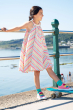 Child wearing the Frugi Tallulah Beach Stripe Trapeze Dress stood in front of railings , the sea can be seen in the background 