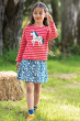 Girl stood on some grass wearing the Frugi eco-friendly organic cotton tori boxy watermelon stripe and unicorn print top 