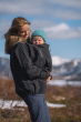 A person wearing the Mamalila Outdoor Explorer Babywearing Jacket - Black, with a child in the front carrier