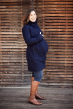 Mamalila Eco Wool Oslo Babywearing Coat in Navy. A navy blue organic boiled wool winter babywearing coat. Side lifestyle view, collar up, with pregnancy insert on front. Wooden slat background.  