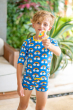 child holding a lollipop wearing the Maxomorra Rainbow Swim Trunks with matching swim top