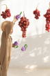 A child holding up an Oli & Carol Grape Rattle Teether Toy with a real bunch of grapes next to it 