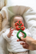 Baby lying down reaching up for an Oli & Carol Tomato Rattle Teether