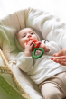 Baby chewing the Oli & Carol Tomato Rattle Teether lying down on a white muslin cloth