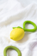 The Oli & Carol Lemon Rattle Teether  placed on a white muslin