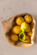 A Oli & Carol Lemon Rattle Teether placed on top of a jute bag full of real lemons