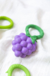 Oli & Carol Grape Rattle Teether pictured on a white muslin cloth