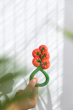 An adults hand holding up the Oli & Carol Tomato Rattle Teether toy