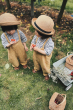 Two boys stood on some grass next to the Olli Ella blue wonder wagon toy, filled with berries and flowers