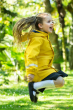 Child jumping in the Frugi Bumblebee Puddle Buster Coat - a solid yellow waterproof rain jacket for children with a navy blue fleece lining. Waterproof to 10,000 HH and made from recycled plastic bottles.