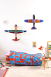The Studio ROOF Deluxe Condition Glider Plane, a huge cardboard model plane with geometric patterns and bright colours, put together, on a white wall in a bedroom with the other Studio ROOF deluxe plane, above a Childs bed