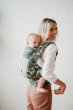 Woman stood in front of a white wall with a baby in a Tula explore baby carrier on her back