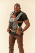 Man stood in front of a beige background looking down at a baby inside a Tula explore mojave baby carrier