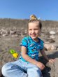 Child sat on some sand at the beach wearing the DUNS Sweden organic cotton short sleeve top in the blue atoll puffin print