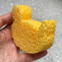 Close up of hand holding A Slice of Green plastic-free duck shape bath sponge over some bubbles