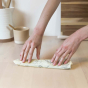 Close up of hands rolling a small Abeego beeswax food wrap on a kitchen counter