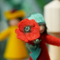 A close up of a poppy flower held in the hand of the Ambrosius poppy boy felted figured 