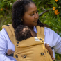 Tula - A woman is outdoors and carries a child on her chest wearing a Hemp Explore Baby Carrier - Citrine.