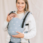A woman carries a child on her chest wearing a Tula - Harbor Skies - Free To Grow - Baby Carrier.