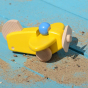 A Bajo Plane With Pilot in a yellow colour way placed on a blue coloured wooden surface in the sunlight. Sand is scattered around the plane