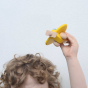 A child holding the Bajo Plane With Pilot in a yellow colour up above their head. They are standing against a white wall