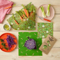 Pieces of fresh vegetables laid out on beeswax food wrap sheets in the land print from the Beeswax Wrap Company on a wooden table