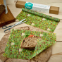 The beeswax wrap co plastic free meadow food wrap rolling up a sandwich on a wooden worktop