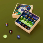 Billes & Co recycled glass Magic Forest marbles mini set open on a dark green background with some coloured marbles scattered in front of the box