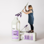Bio D eco-friendly vegan lavender laundry liquid 1L bottle and conditioner 1 Litre bottle, with a woman stood on top of the conditioner bottle, trying to put purple lavender flowers into the laundry liquid bottle