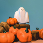 Bumbu hand carved Wooden Ghost toy, with small holes for eyes and a white, sheet-like body, posed among Bumbu wooden toy pumpkins.