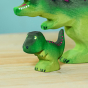 Wooden toy baby T-Rex in vibrant shades of green and purple. The baby T-Rex stands upright in a forward stance. The toy has painted eyes, claws, and body detail. The baby T-Rex stands next to an adult version of the toy for a reference of scale.