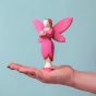 Bumbu Wooden Blossom Fairy. A Radiant and vibrant fairy figure with arms and hands outstretched in front of them. The Bumbu Blossom Fairy wears a bright pink painted dress with small red dot trim, bright pink wings with small red dots at the tips, pink sh