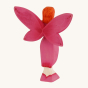 The back of the Bumbu Wooden Blossom Fairy. A Radiant and vibrant fairy figure with arms and hands outstretched in front of them. The Bumbu Blossom Fairy wears a bright pink painted dress with small red dot trim, bright pink wings with small red dots at t
