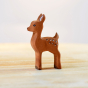 Side view of the Bumbu eco-friendly wooden fawn toy animal stood on a light wooden work top in front of a white background